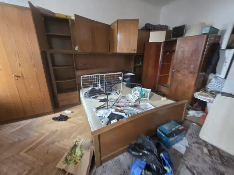 Entrümpelung 1070 Wien Neubau: Zimmer mit alten Holzschränken und vollgeräumtem Bett vor der Räumung
